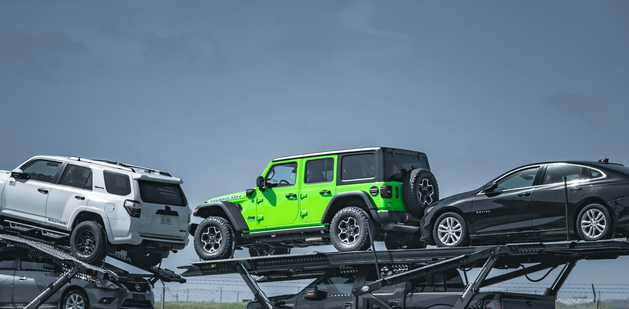 An SUV and a four-door off-roader loaded on the deck of a car carrier against an open sky.