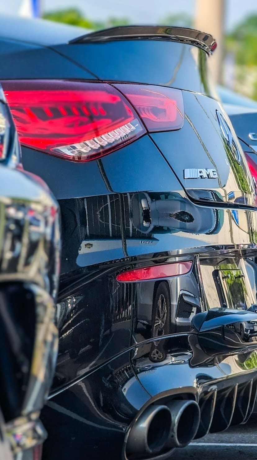 The rear quarter of a delivered performance saloon standing on a dealership lot, tail light and exhaust in close detail.