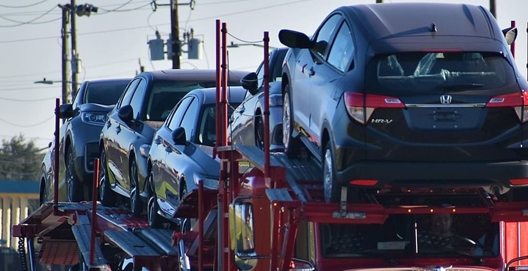 New vehicles standing on the upper deck of a car carrier, held on the steel rails above the cab.