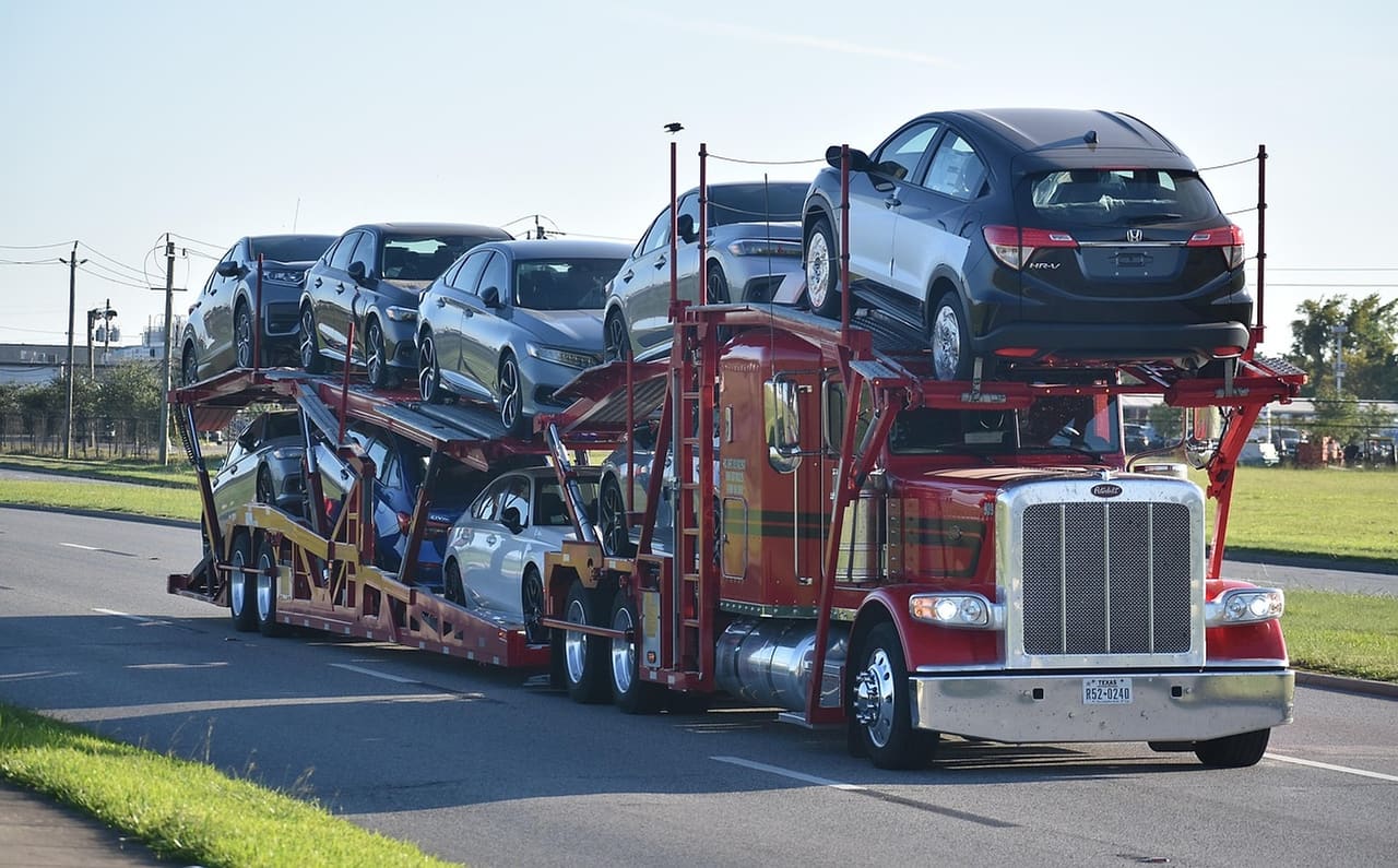 A loaded auto-transport rig on the road at golden hour, cars stacked across both decks behind a conventional cab.