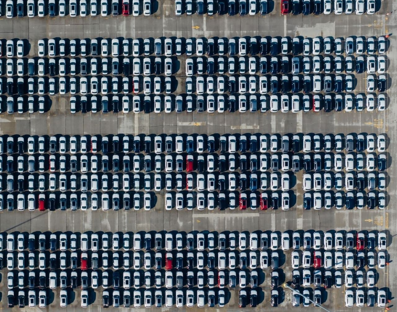 Ranks of new vehicles standing nose to tail in a staging yard, seen from above.
