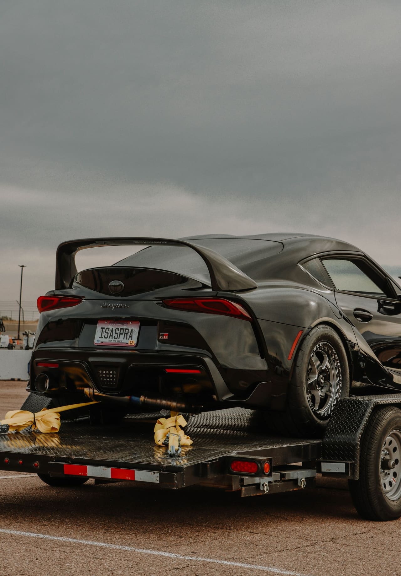 A sports car secured on a transport deck, wheel straps drawn tight through the tie-down rails.